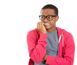 Closeup portrait of nervous, stressed young nerdy guy man in panic and fear, biting fingernails looking anxiously craving something isolated on white background. Negative emotion expression feeling